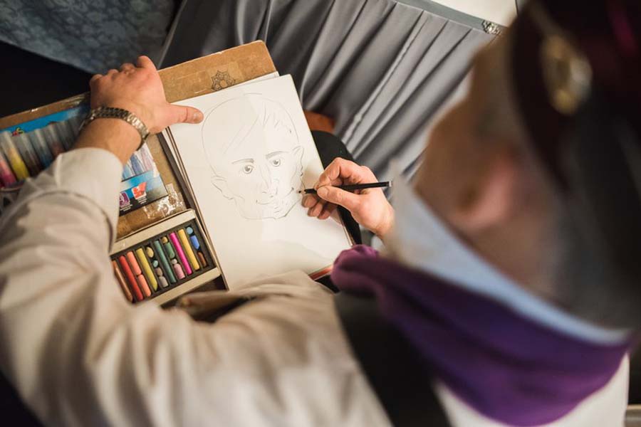 Шаржист Мишель рисует шарж млодого человека
